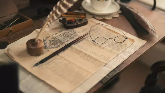 Mesa con taza y platillo de porcelana al lado de la portada del periódico histórico con bolígrafos tradicionales y anteojos de lectura en la parte superior