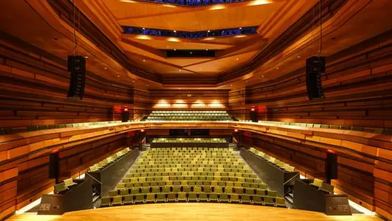  Concert hall stage facing rows of seats in the back with carved wooden ceiling with subdued lighting