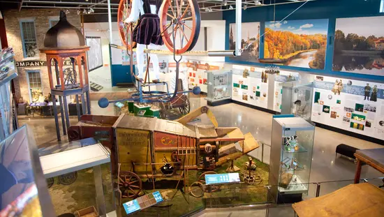 Rücken eines Mannes, der hoch zwischen 2 großen historischen Wagenrädern steht und von Pioniermöbeln und Fotos an den Wänden umgeben ist