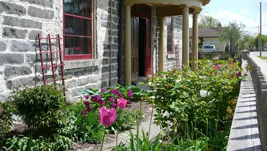 Angle view of old gray brick building with portico at front entrance and tulip garden along front wall