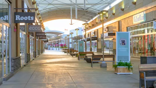 Very long indoor mall with row of benches down middle of aisle and many stores along each side disappearing into the distance