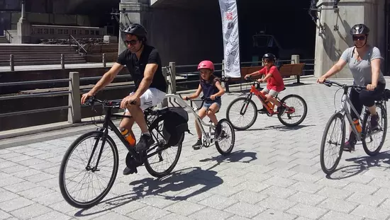 遺産の手すりと高い橋を通過する広い灰色のレンガの小道で自転車に乗る男性と女性と2人の子供