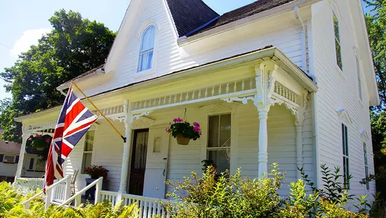 Large old white clapboard house with rectangular white portico across front projecting Canadian flag flying over front gardens
