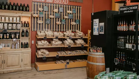 작은 통이 앞에 있고 사이다 병과 수제 빵 및 기타 병의 양쪽 벽에 선반이 있는 매장 내부 코너