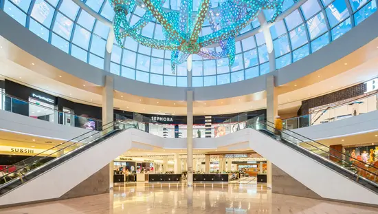 Centre commercial circulaire à deux étages avec vitrines de magasins et éclairé par de nombreuses lumières miniatures colorées sur des tubes suspendus depuis un immense plafond en dôme de verre.