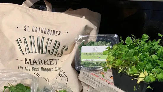 Farmers Market canvas bag on table with 2 cartons of eggs and several potatoes and packages of various green vegetables