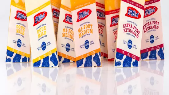 Neuf emballages étiquetés de fromages de couleurs orange et jaune en alternance alignés de façon angulaire sur d'étincelantes tables blanches réfléchissantes.