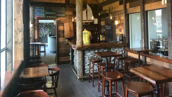 木製のテーブルとスツールと椅子とバーが後ろの角にあり、従業員がボトルの棚に面している素朴な木製レストラン