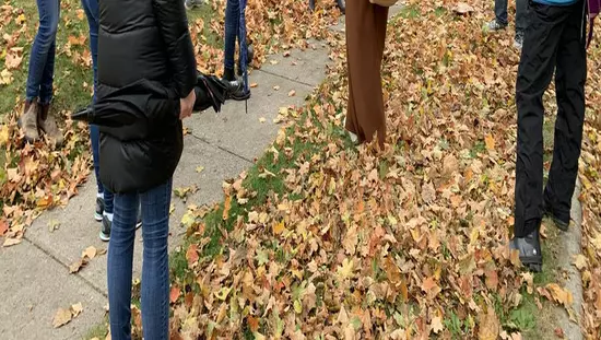 Huit personnes debout sur le terrain d'une ancienne maison sur un tapis de feuilles d'automne et qui regardent un guide touristique qui s'adresse à eux.