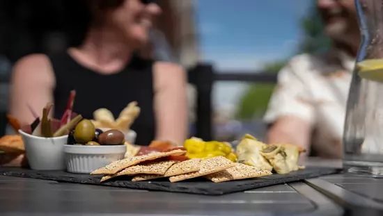 Schwarzes Tablett mit kleinen Schalen aus Rhabarber und Oliven und Crackern und Fingerfood neben einer großen Flasche Wasser mit Zitronenscheiben