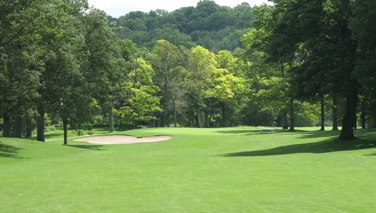 Extensive green golf course lawn with sand trap in front of walkway in foreground and large green forest beyond