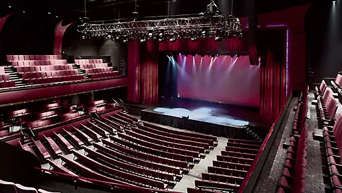 Rows of wine-coloured seats in theatre on both main floor and balconies facing empty stage with entire room softly lit
