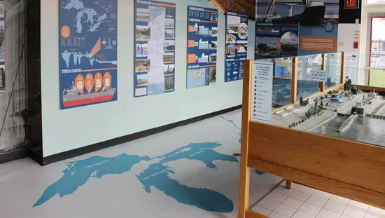 On left wall-size screen of maps and photos and on right large photo of ship in lock above a scale model of lock facility