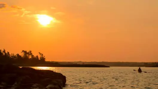 일몰 무렵 물 위에서 카약을 타는 사람.