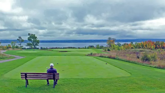 한 남자가 골프장의 그린을 내려다보는 벤치에 앉아 있다.