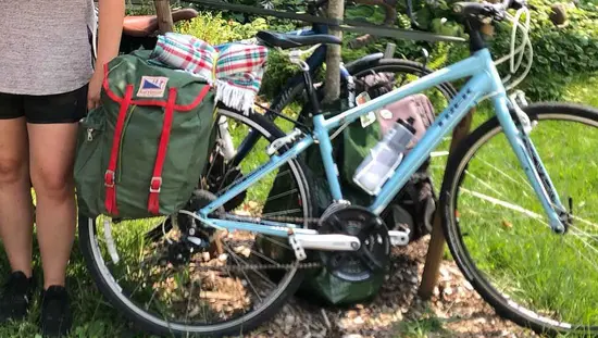Un homme et une femme, tous deux portant des casques de vélo, posent avec un vélo appuyé contre un arbre