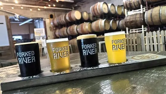 Un vuelo de 4 cervezas con cervezas claras y oscuras con barriles en el fondo.