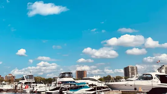 Ein strahlend blauer klarer Himmel mit ein paar Wolken über einer Vielzahl von Luxusbooten, die an einem Yachthafen festgemacht sind