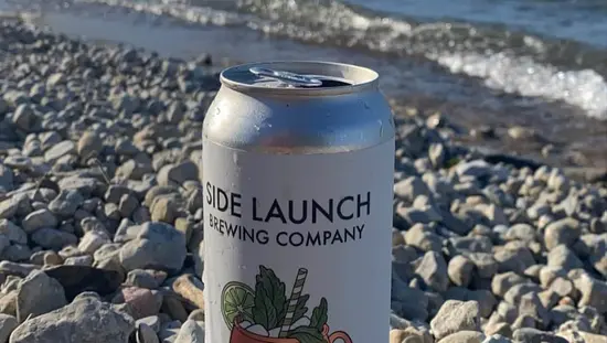 A can of beer resting on pebbles with a lake in the background