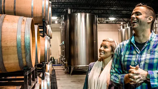 Un couple admire une pile de tonneaux de vin dans une cave viticole