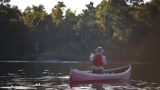 A man casting his line from a boat on a lake