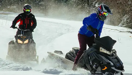 2人のスノーモービル乗りが雪の中を走る