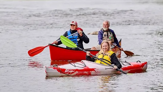 A girl in a kayak in front of two men in a canoe