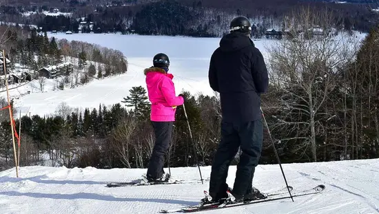 Two people getting ready to ski, while look down at the slopes.