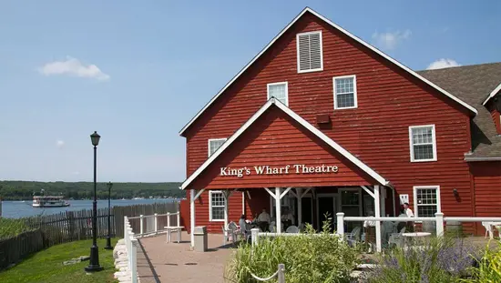 People enjoying a conversation outside of a red, wooden building that is located beside the waterfront
