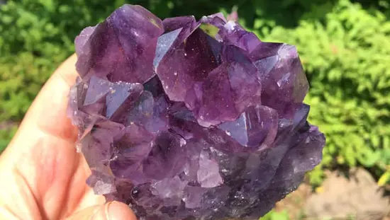 Close-up view of a hand holding an amethyst crystal.