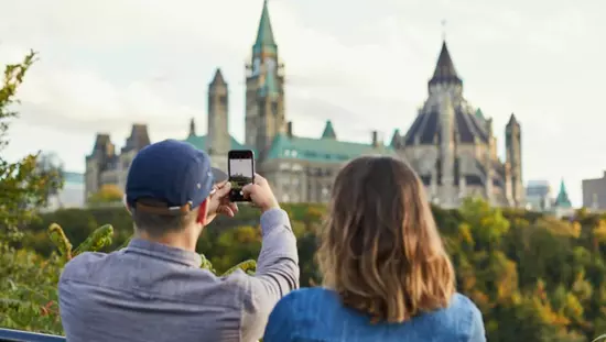 오타와의 의회 언덕에서 사진을 찍고 있는 남자 옆에 서 있는 여성. 