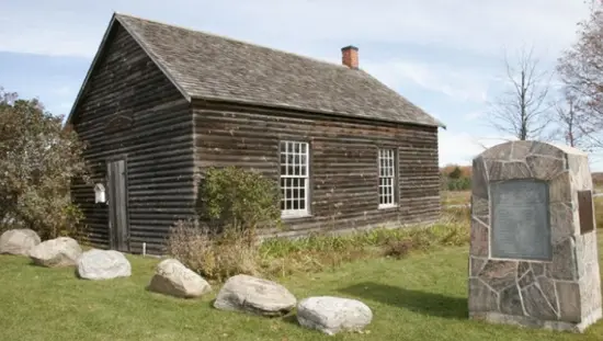 역사적인 통나무 건물 옆에 있는 돌로 덮인 기념패.