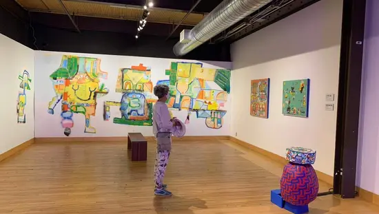 Eine Frau mit einer Maske bewundert die Kunst in einem Raum.