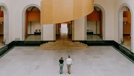 Geräumiger Innenraum der Art Gallery of Ontario mit großen Torbögen, hohen Decken und einer markanten hölzernen Wendeltreppe in der Mitte.