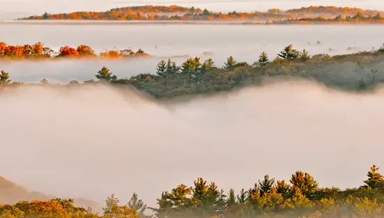  Im Herbst zieht Morgennebel durch die bewaldeten Hügel des Algonquin Provincial Parks, durch die mehrere Lagen bunter Bäume hervorschauen.