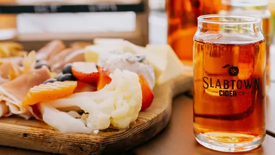 Two pints of amber beer on a wooden table beside a charcuterie board at Slabtown Cider Co. restaurant in Uxbridge.