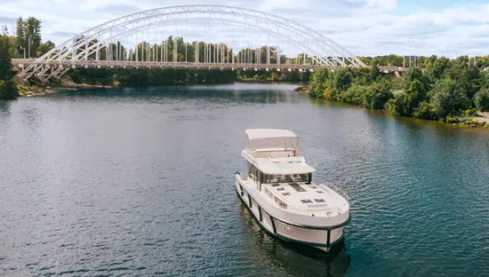 Eine kleine Gruppe genießt eine Bootsfahrt auf dem Rideau-Kanal, mit einer großen Bogenbrücke und üppigem Grün im Hintergrund unter einem teilweise bewölkten Himmel.