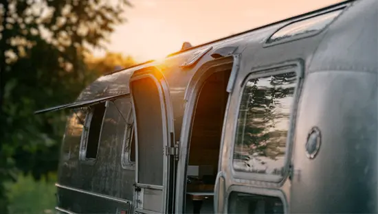  Nahaufnahme eines Airstream-Wohnwagens in einem Waldgebiet außerhalb von Ottawa, während die Sonne hinter den Bäumen untergeht.