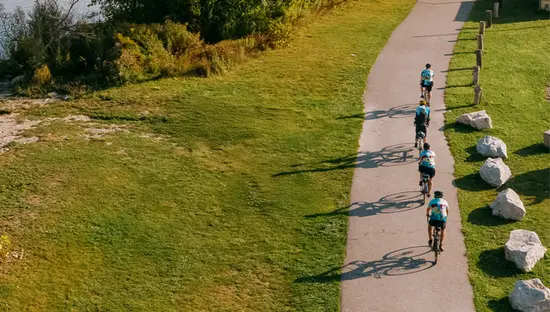 オンタリオ州コリングウッドのジョージアン湾沿いのウォーターフロントの小道をサイクリストたちが走り、遠くに静かなマリーナと帆船の眺めを楽しみます。