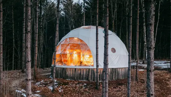 Eine Kuppelhütte, versteckt zwischen immergrünen Bäumen auf der Glen Oro Farm, von oben auf einem gewundenen Pfad mit Flecken schmelzenden Schnees gesehen.