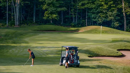 Ein Golfer bereitet sich auf einem sonnigen Fairway im Sault Ste. Marie Golf Club auf seinen Abschlag vor, in der Nähe ein Golfwagen und im Hintergrund ein üppiger Wald.