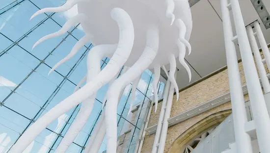 Große weiße Quallenskulptur, die im Glasatrium des Canadian Museum of Nature in Ottawa hängt, mit Spiegelungen auf den Fenstern.