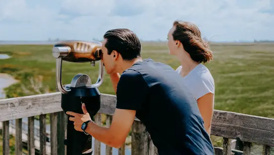 포인트 펠리 국립공원의 전망대에 있는 한 커플. 한 명은 쌍안경을 사용하고, 다른 한 명은 화창한 날 습지와 산책로를 감상하고 있습니다.