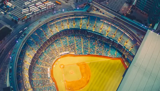  Luftaufnahme der Innenstadt von Toronto in der Abenddämmerung mit dem beleuchteten Rogers Centre-Stadion und der Uferpromenade und den Hochhäusern, die es umgeben.