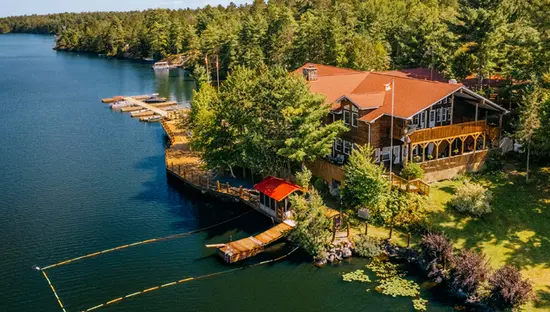 Centre de villégiature Saenchiur Flechey en été, avec pavillon au toit rouge, rivage boisé et quais le long d'un lac paisible du nord de l'Ontario.
