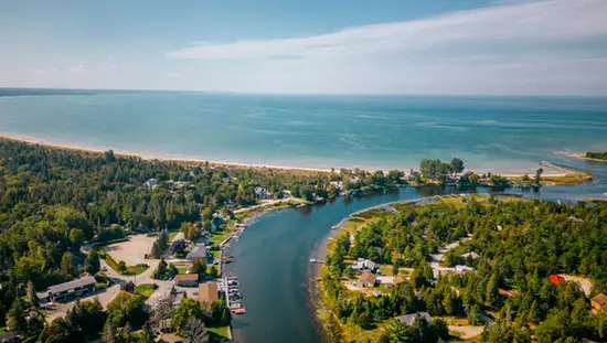 Vue aérienne de la rivière Sauble se jetant dans le lac Huron à Sauble Beach, avec des chalets, une rive sablonneuse et une eau d’un bleu limpide.