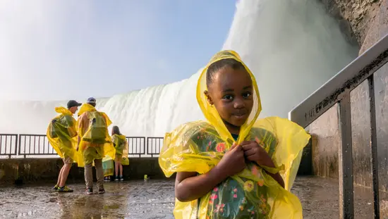 Touristen, darunter ein junges Mädchen, tragen Ponchos, um sich vor dem Nebel der Niagarafälle zu schützen.