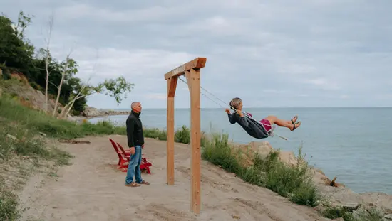 A man pushes a woman on a swing on the sand banks of a beach overlooking Lake Erie.