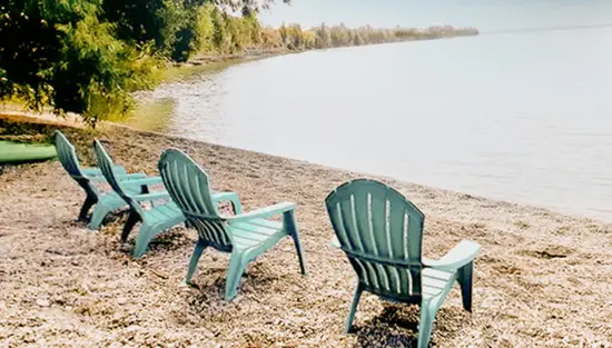 Fauteuils Muskoka turquoise alignés sur la plage de galets du Pebbles Beach Resort, à l’ombre des arbres et face à un lac calme.
