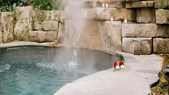 Steam rising from a serene spa pool with stone walls and candles perched on the uneven stone wall at 100 Fountain Spa in Niagara-on-the-Lake.
